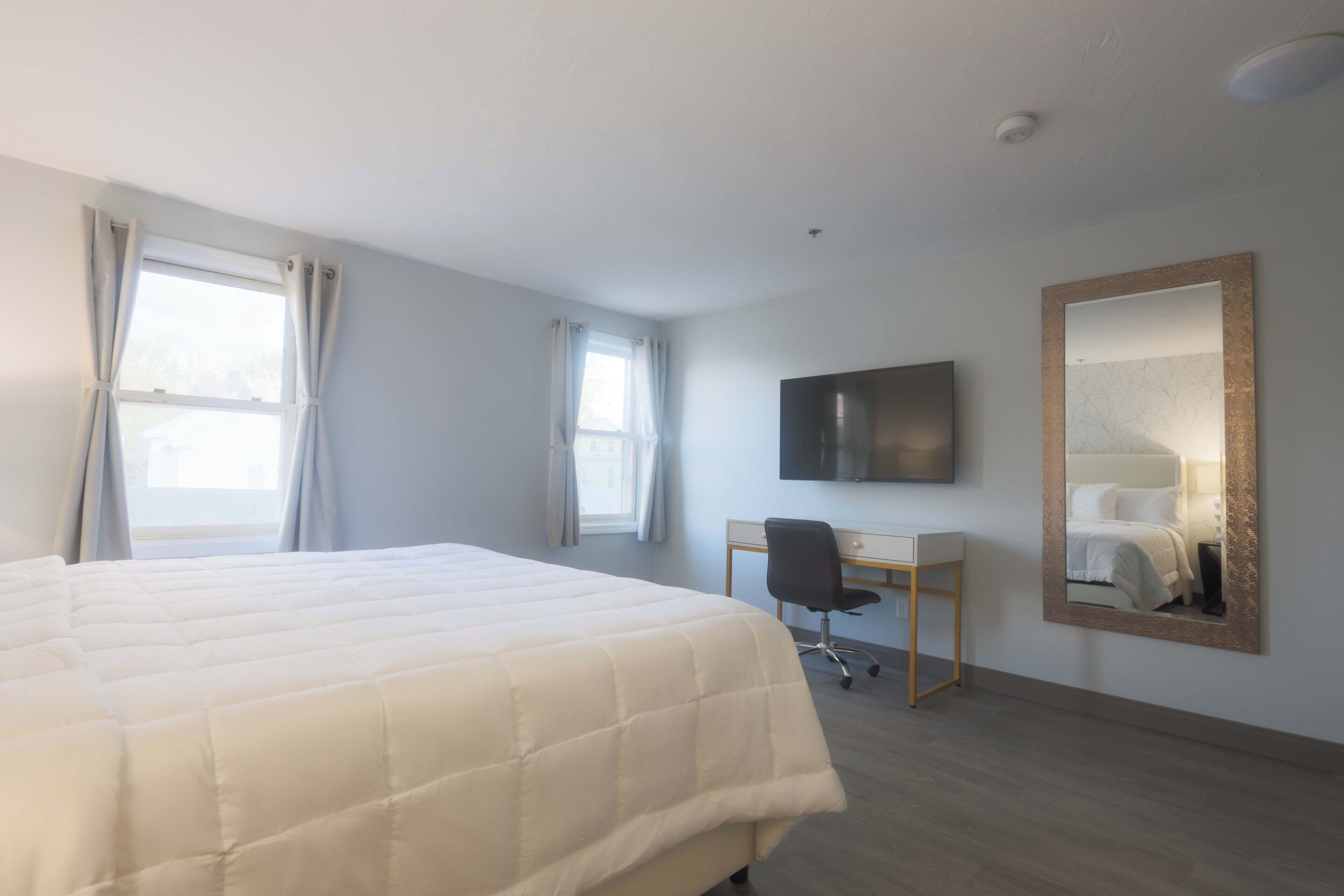 Habitación de hotel con una cama grande, un escritorio, una silla, un televisor de pantalla plana y un espejo en la pared.