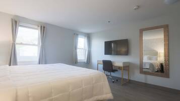 Habitación de hotel con una cama grande, un escritorio, una silla, un televisor de pantalla plana y un espejo en la pared.