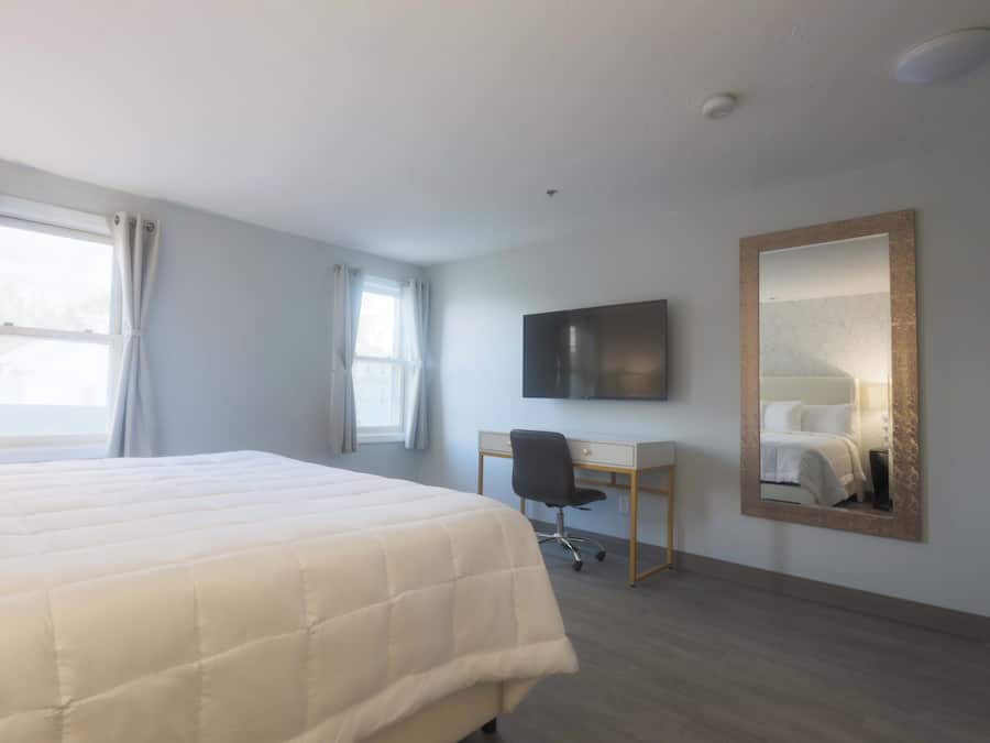 Habitación de hotel con una cama grande, un escritorio, una silla, un televisor de pantalla plana y un espejo en la pared.