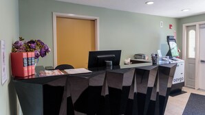 A reception desk with a computer, a printer, and a plant. There is a door and a window in the background. - Westborough Inn (Westborough)