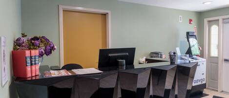A reception desk with a computer, a printer, and a plant. There is a door and a window in the background.