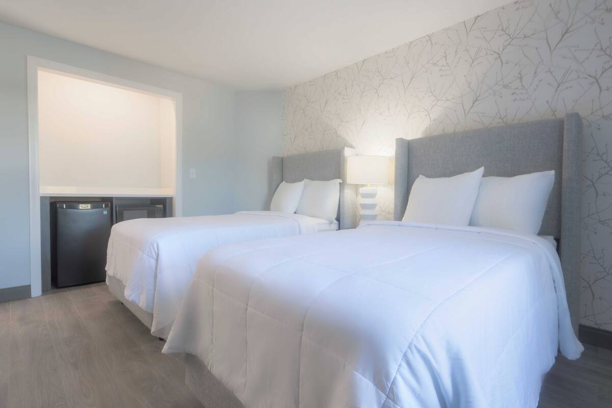 A hotel room with two beds, a desk, and a window.