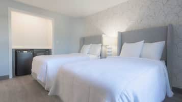 A hotel room with two beds, a desk, and a window.