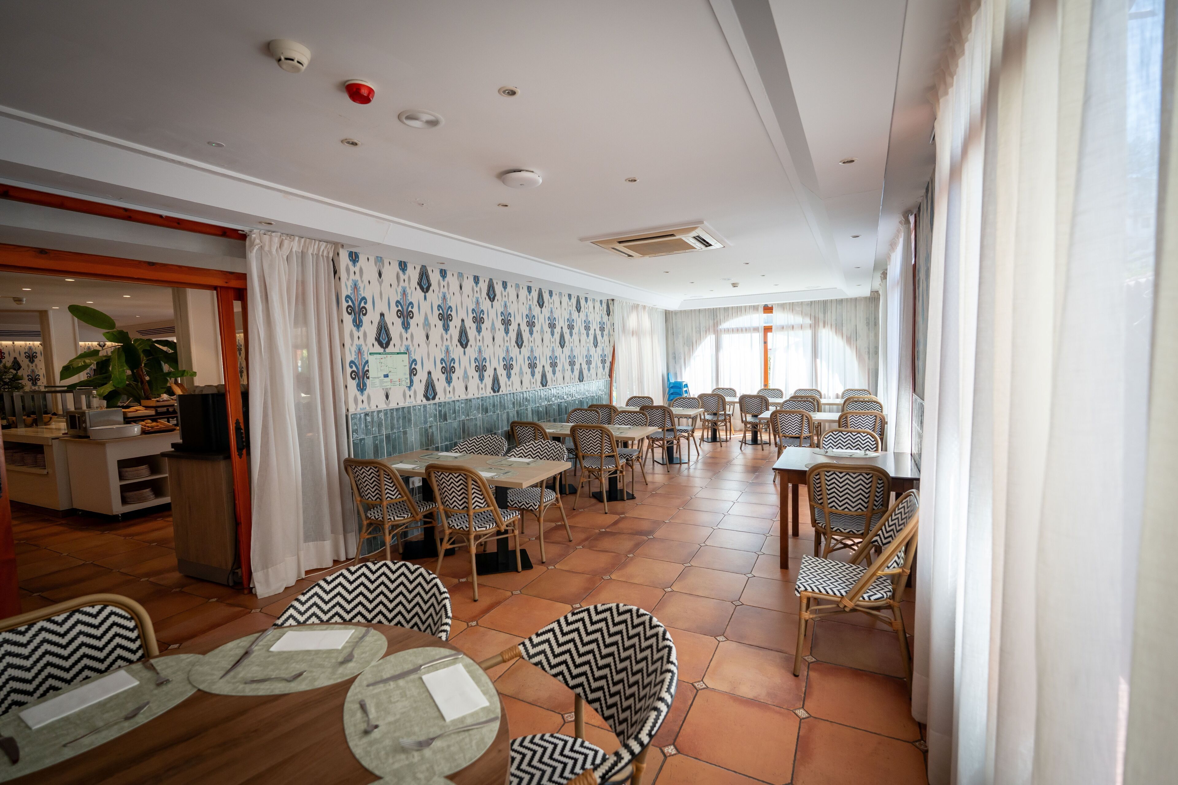 A dining area with round tables and chairs, a kitchen area, and patterned walls.