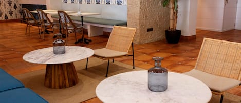 A modern lounge area with round tables, wicker chairs, a bench, and a potted plant.