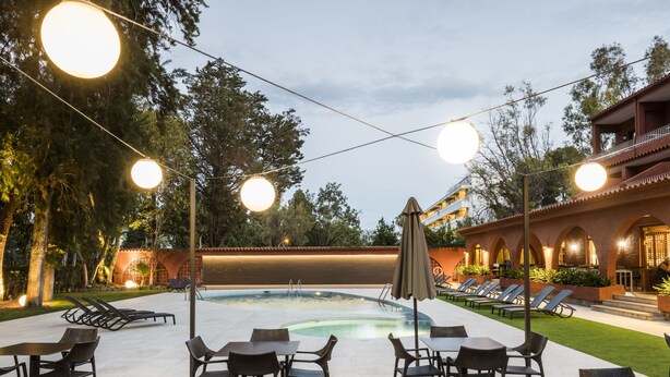 Un área de piscina al aire libre con sillones reclinables, mesas y luces colgantes.