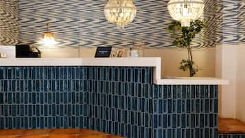 A reception desk with a patterned wall, two chandeliers, and a potted plant.