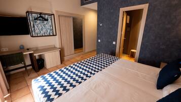 A hotel room with a bed, a desk, a chair, a wardrobe, and a bathroom visible through an open door.