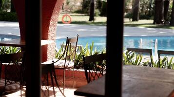 Zona junto a la piscina con mesas y sillas, vista a la piscina y un flotador sobre el césped.