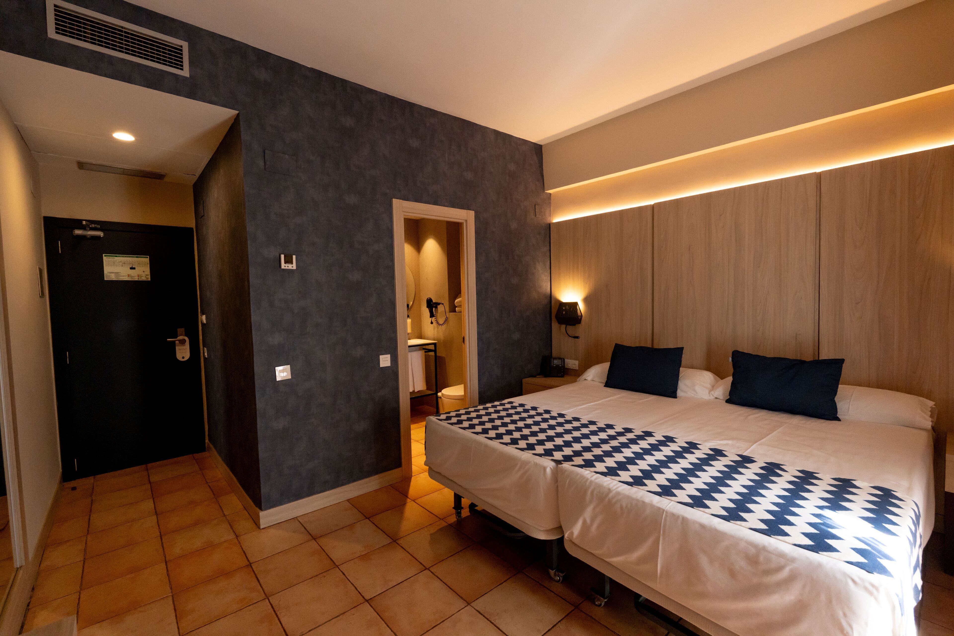 Habitación de hotel con una cama grande, una mesita de noche, un armario y un baño visible a través de una puerta abierta.