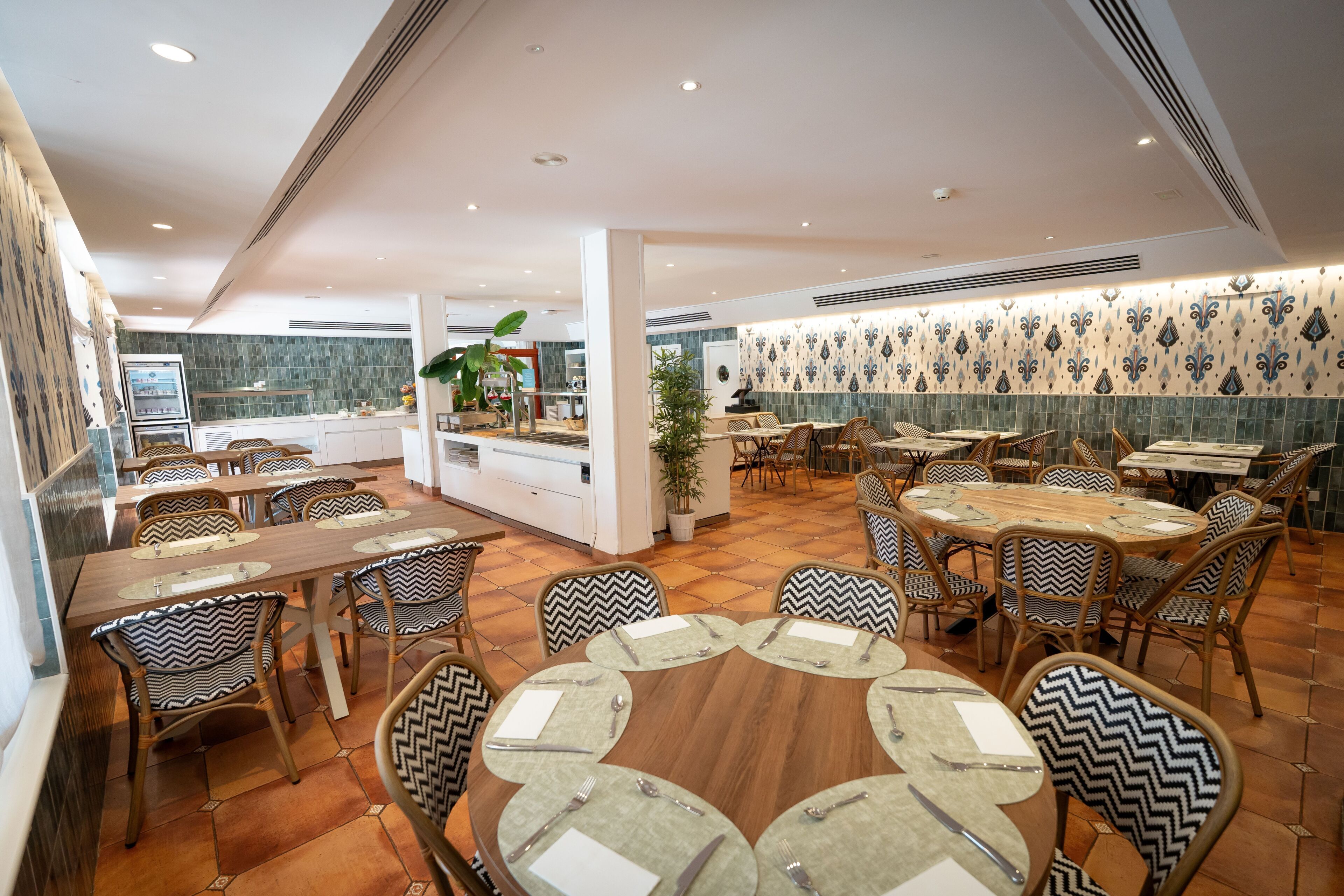 Un restaurant avec des tables rondes, des chaises dotées de coussins à motifs et un mur recouvert de carreaux.