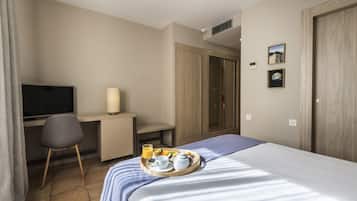 Una habitación de hotel con una cama, un escritorio, una silla, un televisor y una bandeja con alimentos para el desayuno.