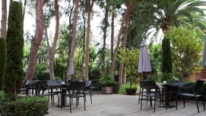 Un patio al aire libre con piso de madera, sillas de mimbre negro y sombrillas moradas.
