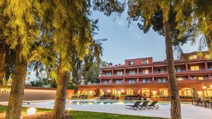 Un hotel con piscina, mobiliario exterior y fachada de color rojo.