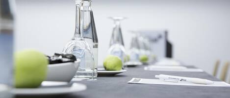 Una mesa de conferencias con cristalería transparente, platos con manzanas verdes y un bolígrafo blanco.
