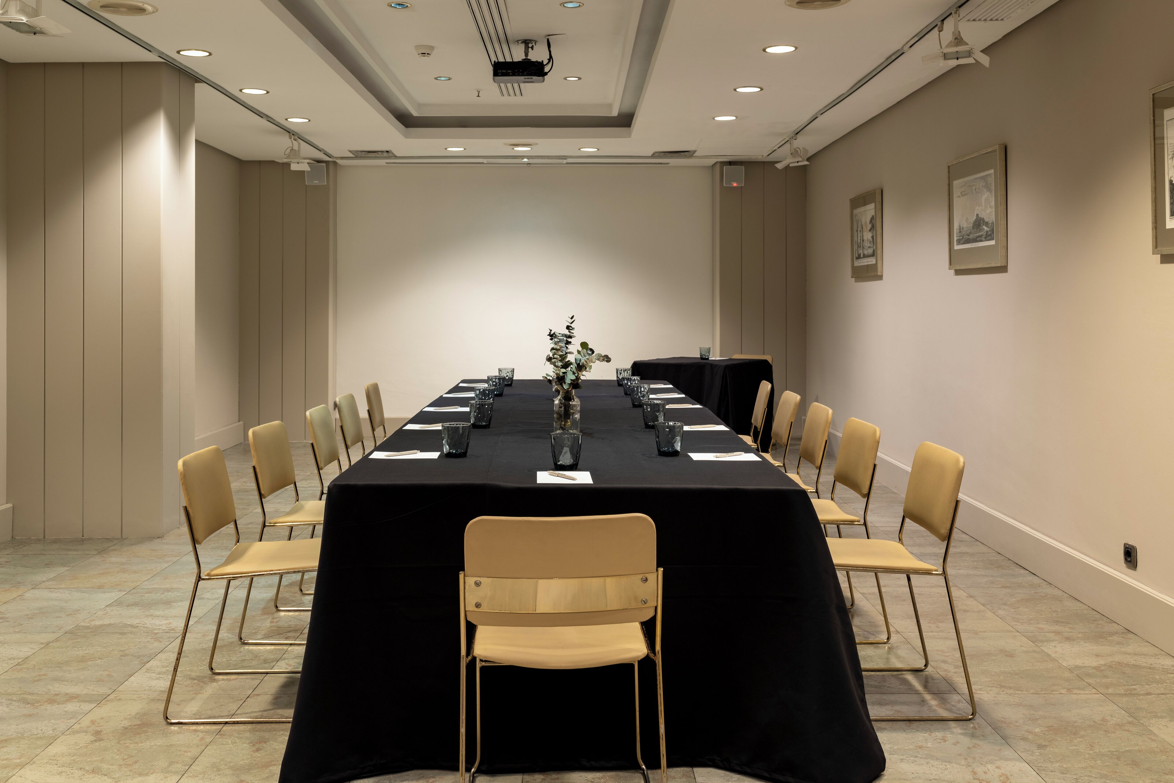 Une salle de conférence avec une longue table, des chaises et un projecteur fixé au plafond.