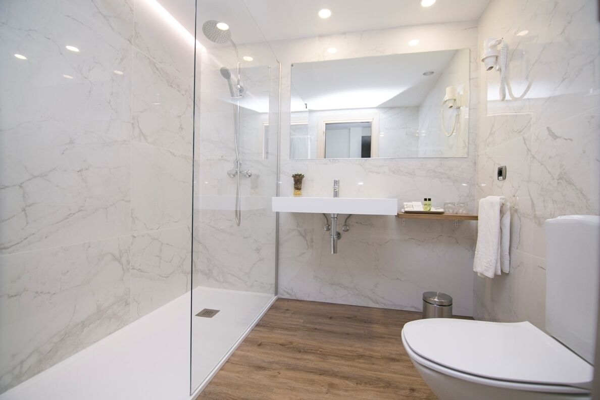 Un baño moderno con cabina de ducha de vidrio, suelo de madera, lavamanos blanco y un inodoro.