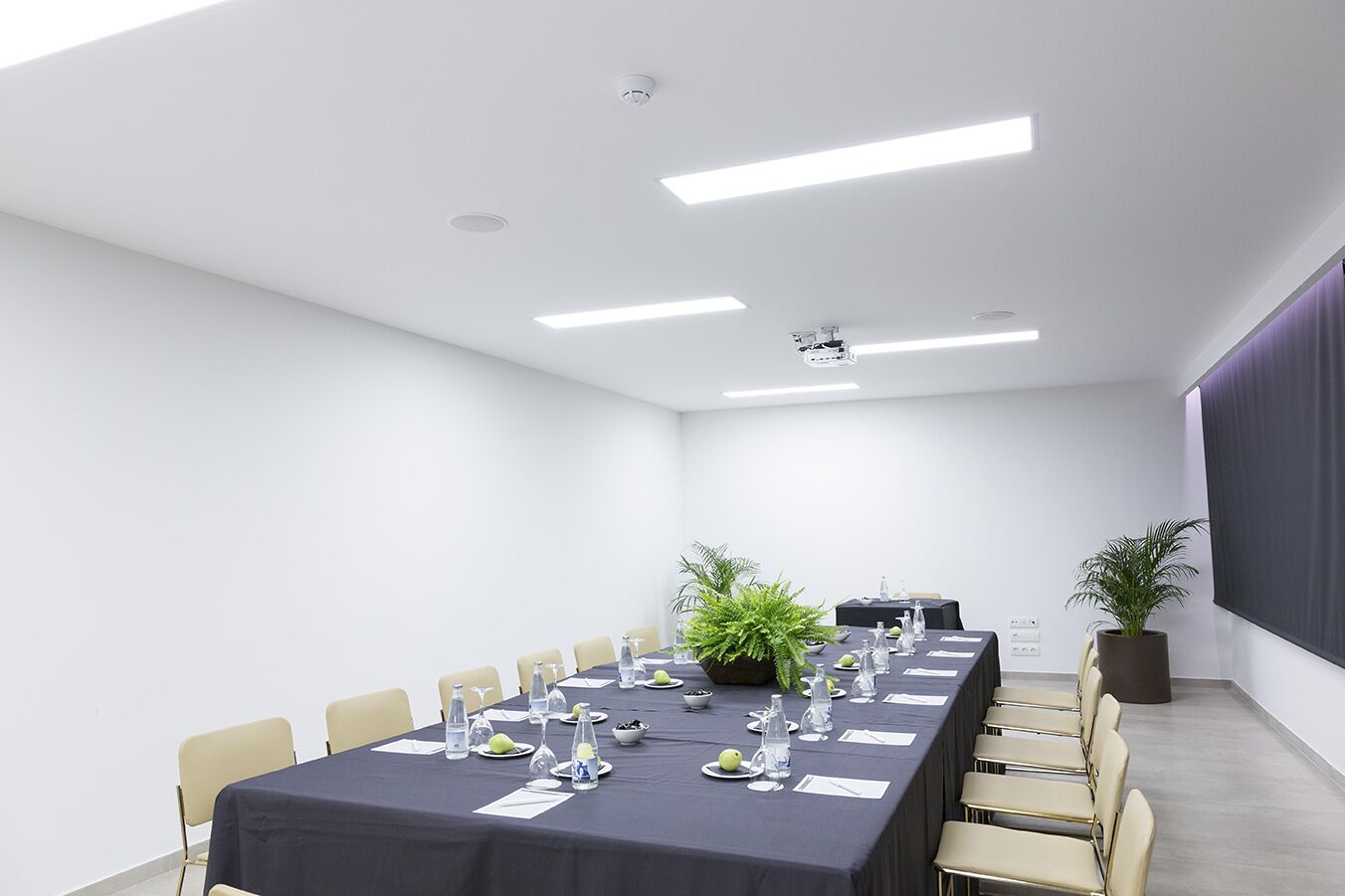 Un salón de conferencias con una larga mesa, sillas, un proyector y una pantalla.