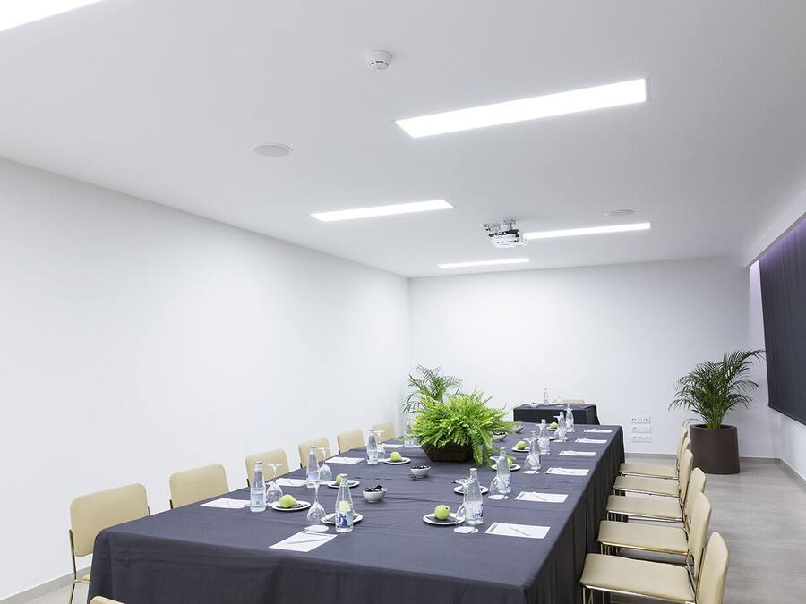 Un salón de conferencias con una larga mesa, sillas, un proyector y una pantalla.