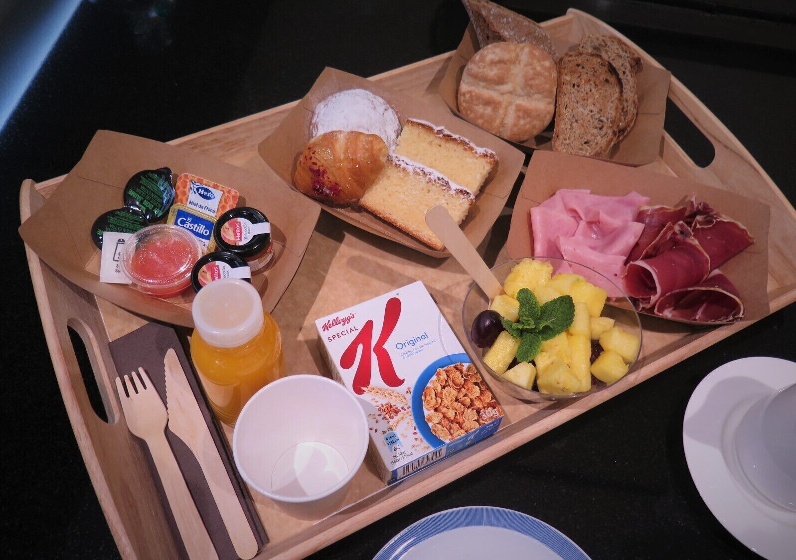 Bandeja de desayuno con pan, bollería, queso, jamón, frutas y cereales.