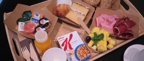 Bandeja de desayuno con pan, bollería, queso, jamón, frutas y cereales.