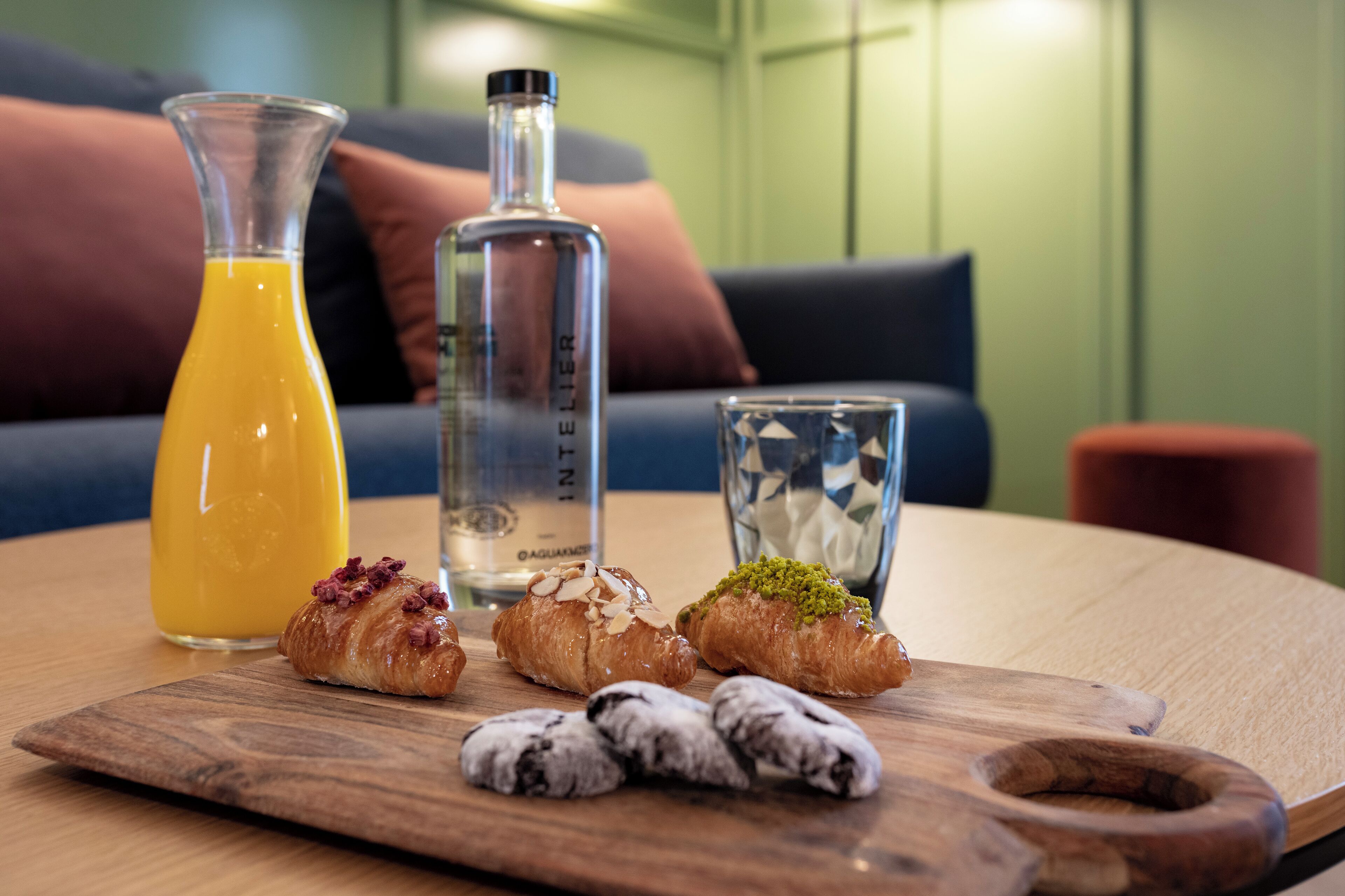 Una mesa de madera con pasteles, una botella de vidrio y un vaso de jugo de naranja.