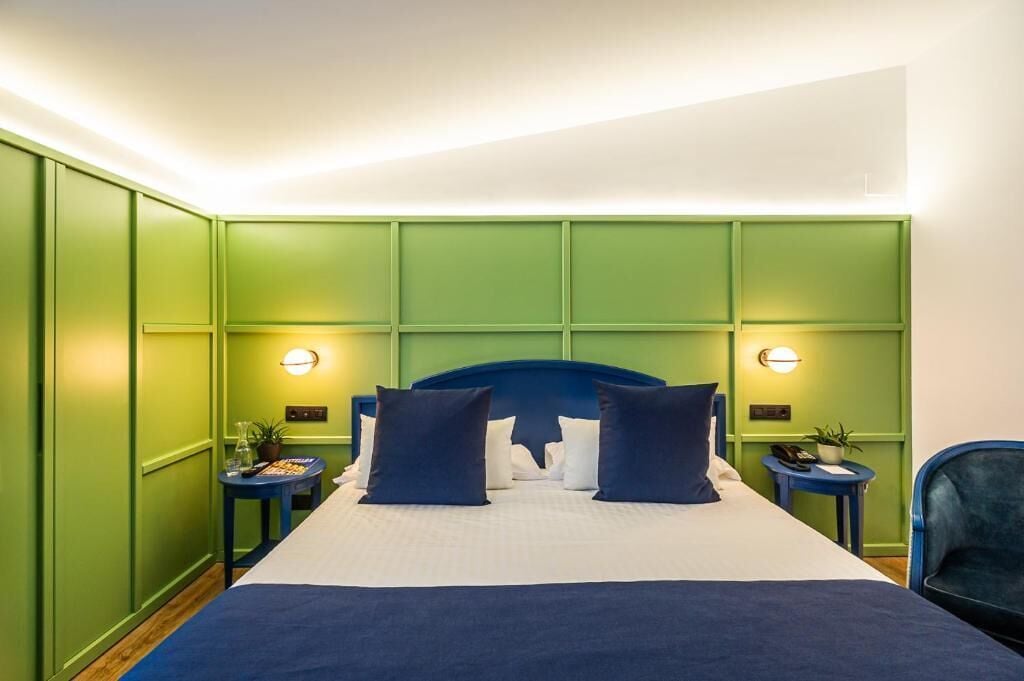 A hotel room with a large bed, green walls, two bedside tables with lamps, and a blue chair.