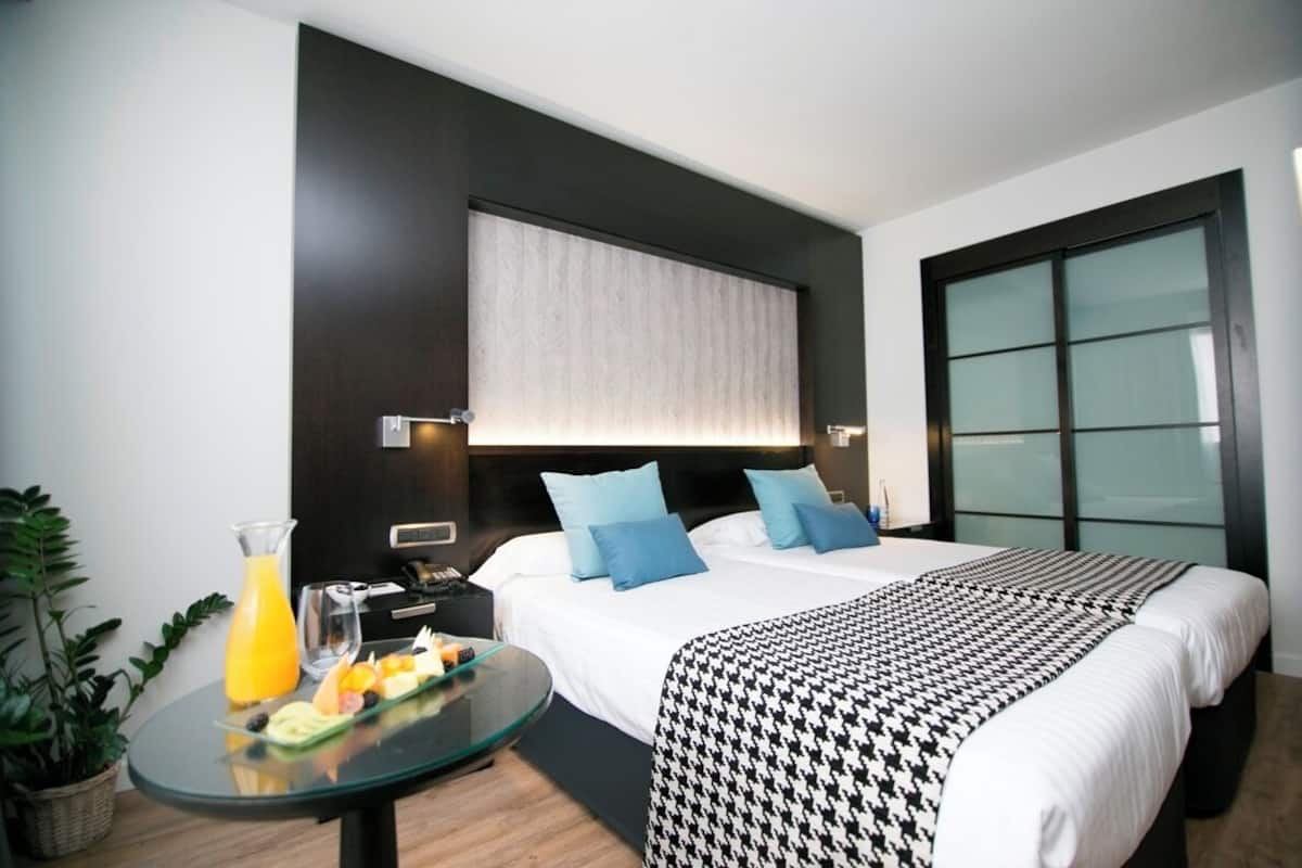 A hotel room with a bed, bedside table with breakfast, a large window, and a potted plant.