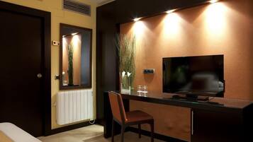 Una habitación de hotel con cama, escritorio y silla, televisor y radiador.