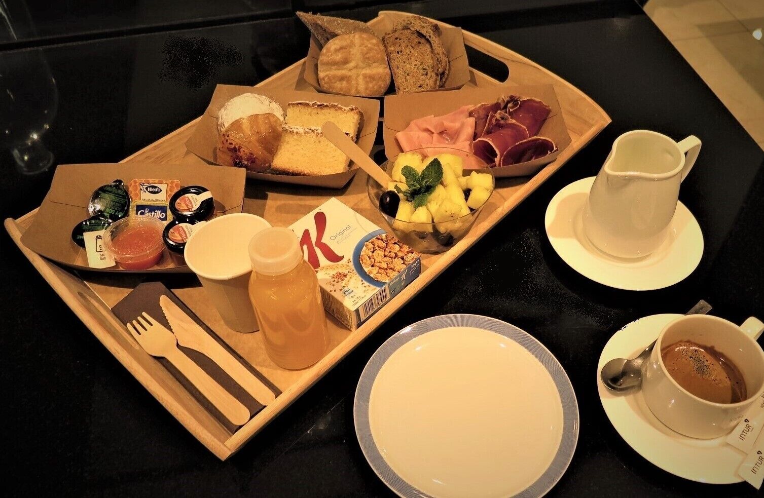 A breakfast tray with pastries, fruits, cheese, and a coffee cup.