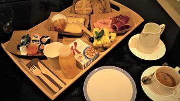 A breakfast tray with pastries, fruits, cheese, and a coffee cup.