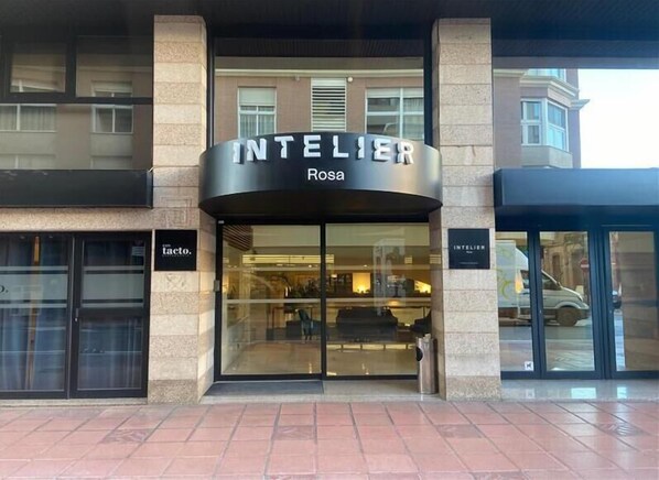 The exterior of a hotel named "INTELLIER Rosa" with a modern design, featuring large glass windows and a stone facade.
