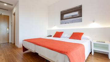 Een hotelkamer met een groot bed, wit beddengoed en een rode deken. Er hangt een schilderij aan de muur, en er is een nachtkastje.