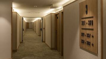 A hotel hallway with numbered doors, carpeted floors, and a wooden wall panel with room numbers.