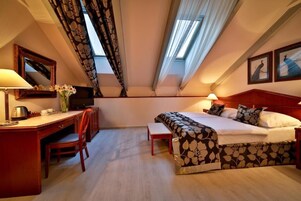Quarto de hotel com cama, escrivaninha, cadeira e televisão.