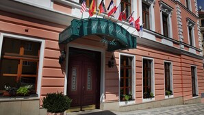 L’entrée d’un hôtel, avec une arche imposante ornée de plusieurs drapeaux, une porte rouge et des plantes en pot.