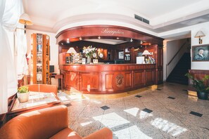 A reception area with a curved wooden desk, a clock, and a flower vase. - Hotel Carlton (Prague)
