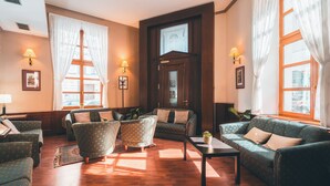 Un salon spacieux doté d’un plancher en bois, d’une grande fenêtre avec des rideaux et d’une porte en bois foncé.
