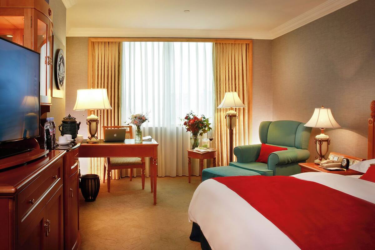 Habitación de hotel con cama, escritorio, laptop, televisor y una silla.