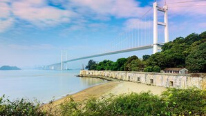A large suspension bridge over a calm body of water, with a stone wall and greenery in the foreground. - Grand Noble Hotel (Dongguan)