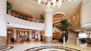 A spacious lobby with a grand staircase, a reception area, and multiple seating arrangements. - Grand Noble Hotel (Dongguan)