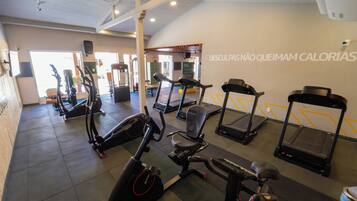 Academia com diversos equipamentos de cardio, incluindo esteiras e bicicletas ergométricas, e uma parede com frases motivacionais.