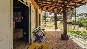 A covered outdoor area with a bench, a door, and a view of palm trees and a lawn. - Sauipe Terra Resort - All Inclusive (Mata de São João)