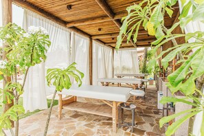 An outdoor covered patio with stone flooring, wooden furniture, and lush green plants. - Sauipe Terra Resort - All Inclusive (Mata de São João)