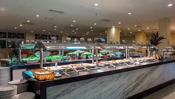 A buffet with various food stations, a counter with stacked plates, and a large decorative plant.