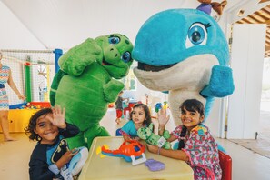 Quarto com área de recreação, incluindo uma mesa com brinquedos e um dinossauro inflável grande.