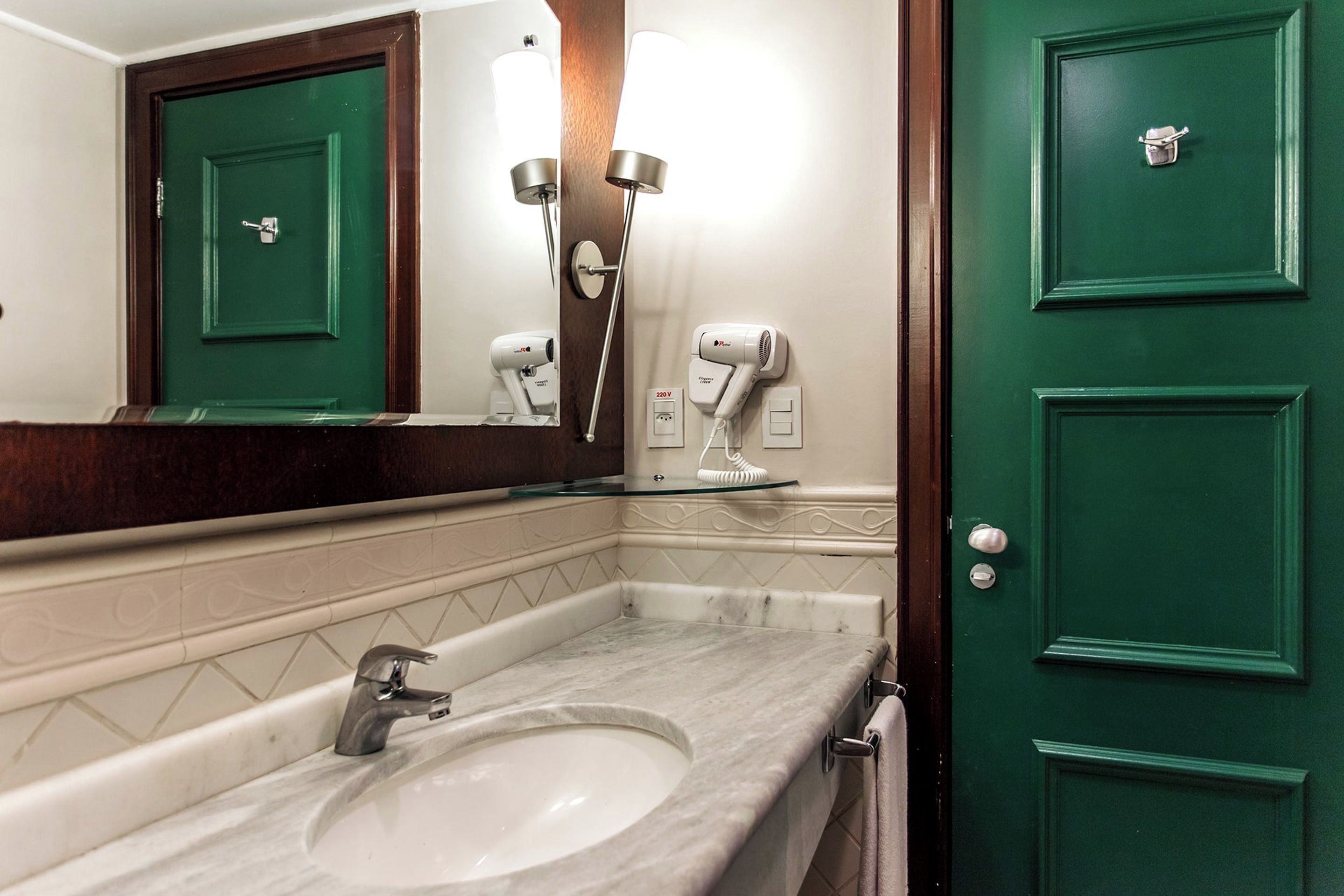 Un baño con una puerta verde, un espejo, un lavamanos y dos secadores de pelo.