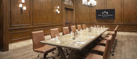 Une salle de conférence avec une longue table, des fauteuils en cuir et un lustre.
