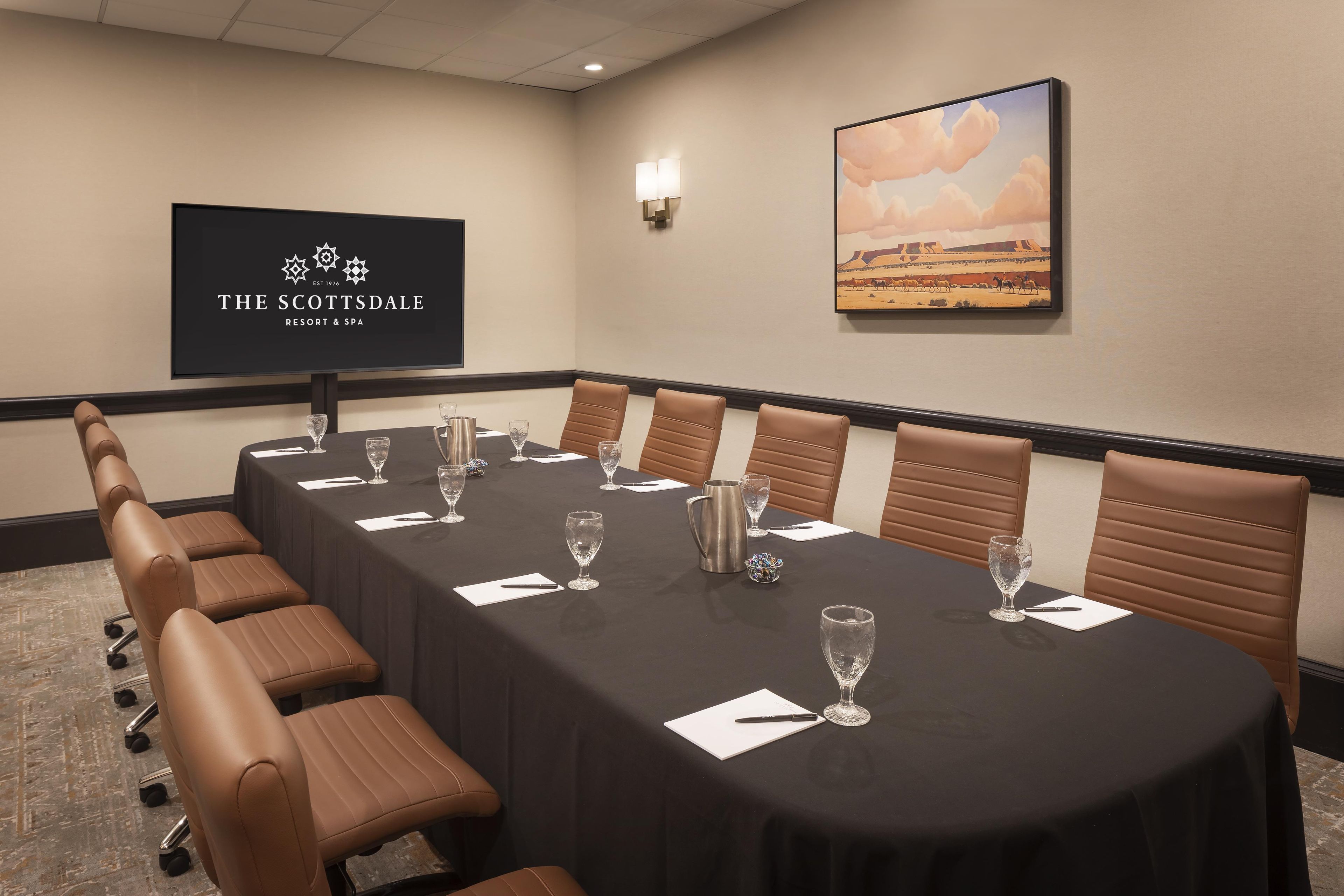 Una sala de conferencias en The Scottsdale Resort & Spa con una mesa larga, sillas de cuero marrón y una pantalla proyectora mostrando el logo del resort.