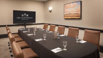 Una sala de conferencias en The Scottsdale Resort & Spa con una mesa larga, sillas de cuero marrón y una pantalla proyectora mostrando el logo del resort.